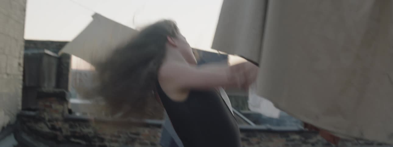 A woman dances on a rooftop in a city