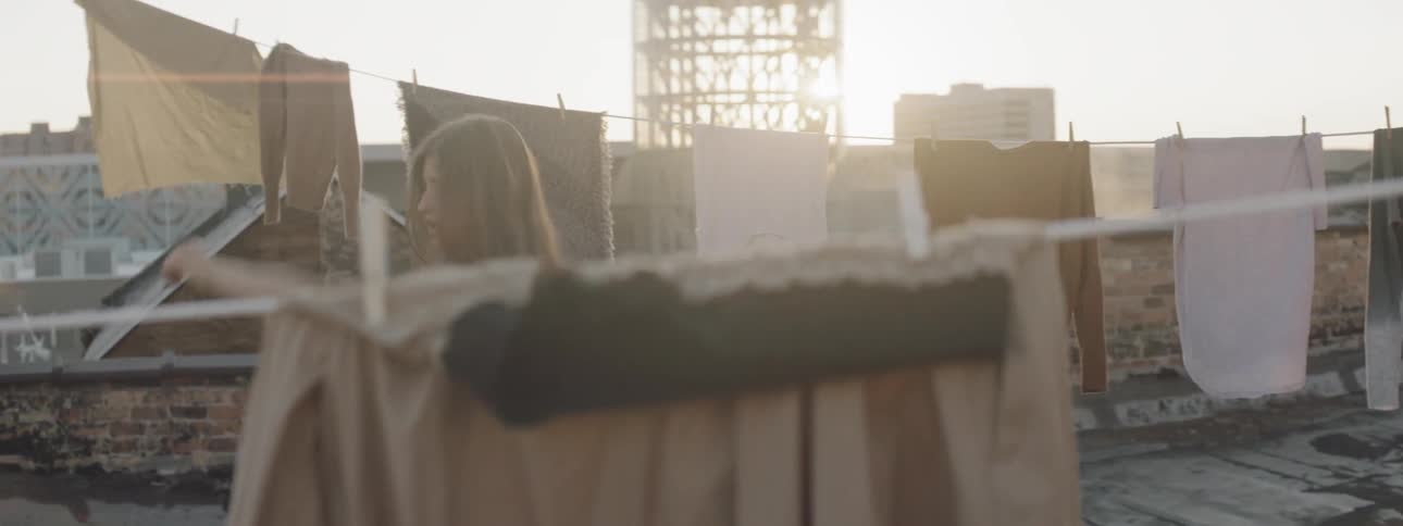 A woman dances on top of a roof with clothes hung all around