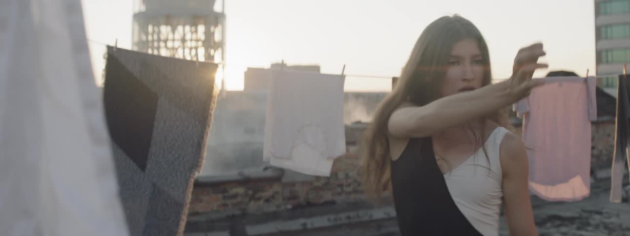 A white woman dances in between clotheslines on the roof of a building