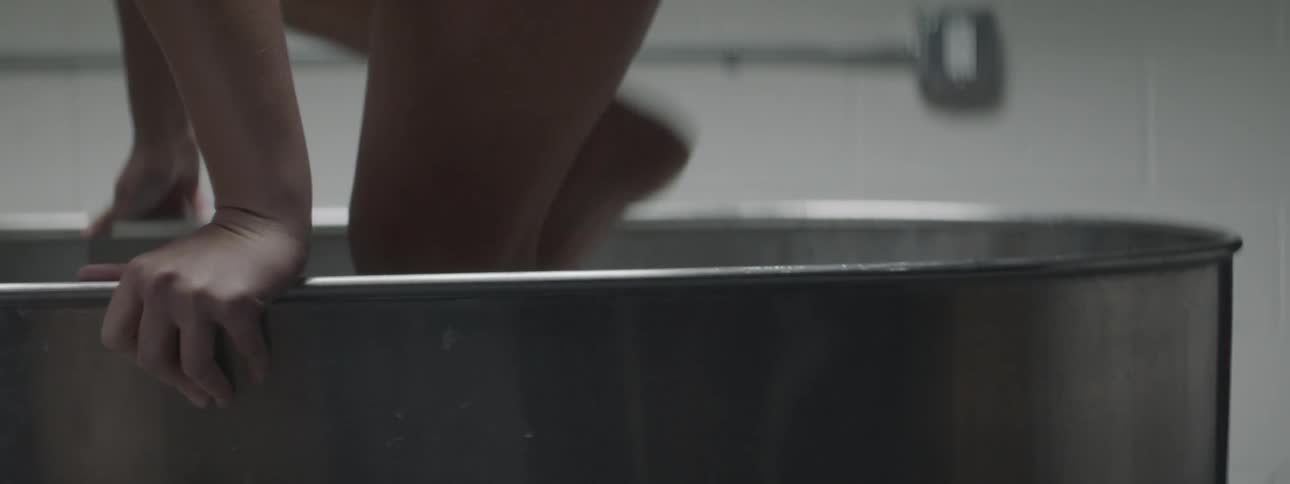 Woman steps into large metal tub and sits down