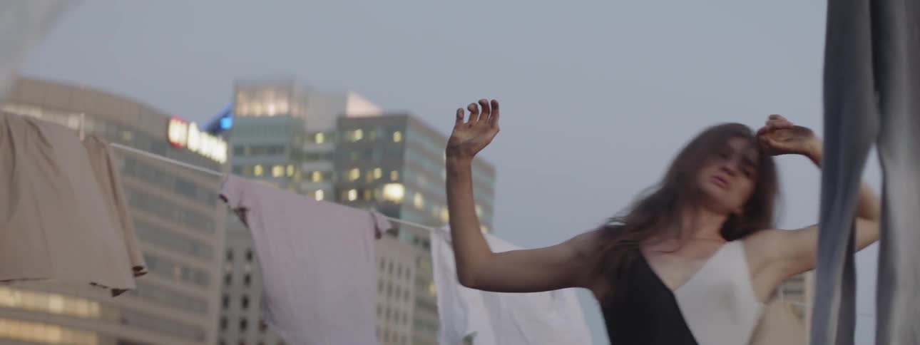 A woman dances on a rooftop surrounded by laundry on the drying line