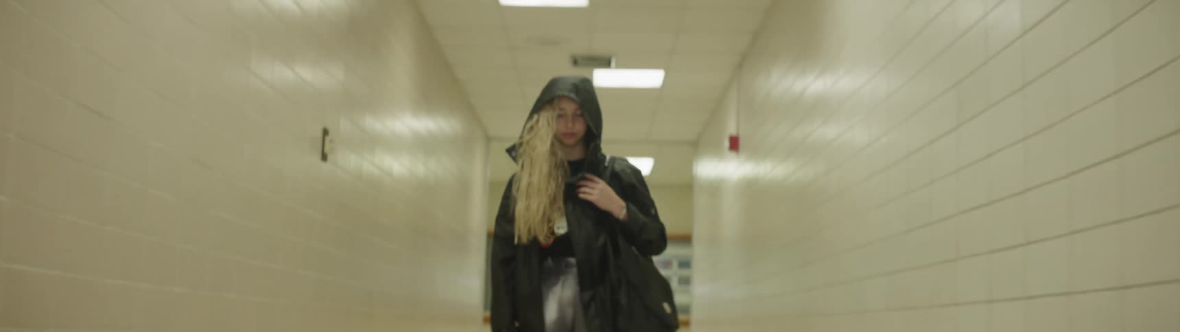 The camera goes down a hallway to look at a woman standing still