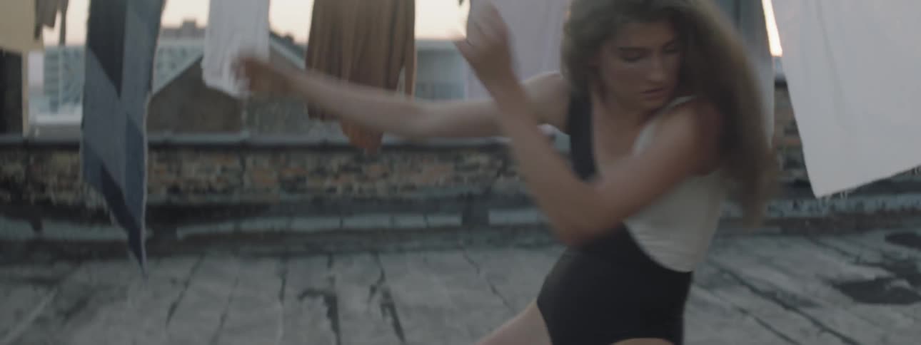 A woman dances on a rooftop with clothes hanging around her