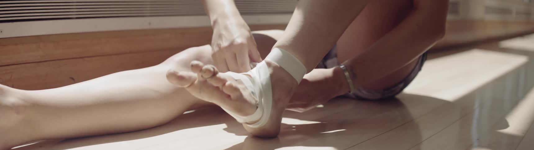 A woman in a dance studio sitting on the floor taping up her foot