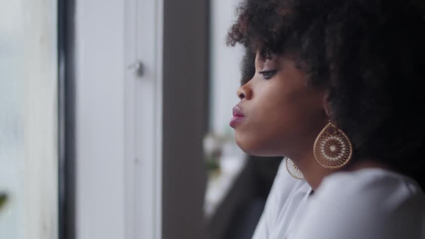 A woman shrugs her shoulders as she looks out the window