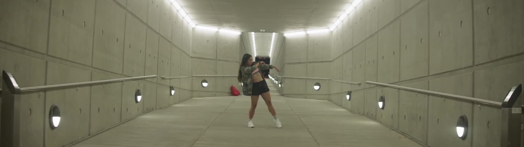 A woman dances in a brightly lit cement corridor