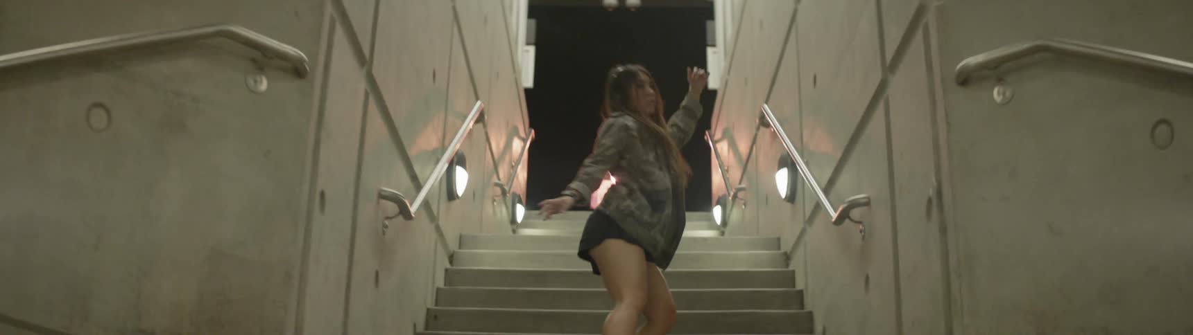A woman in a train station stairway dancing while listening to music on her headphones