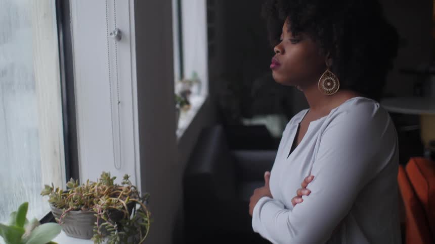 A woman walks over to a window and folds her arms