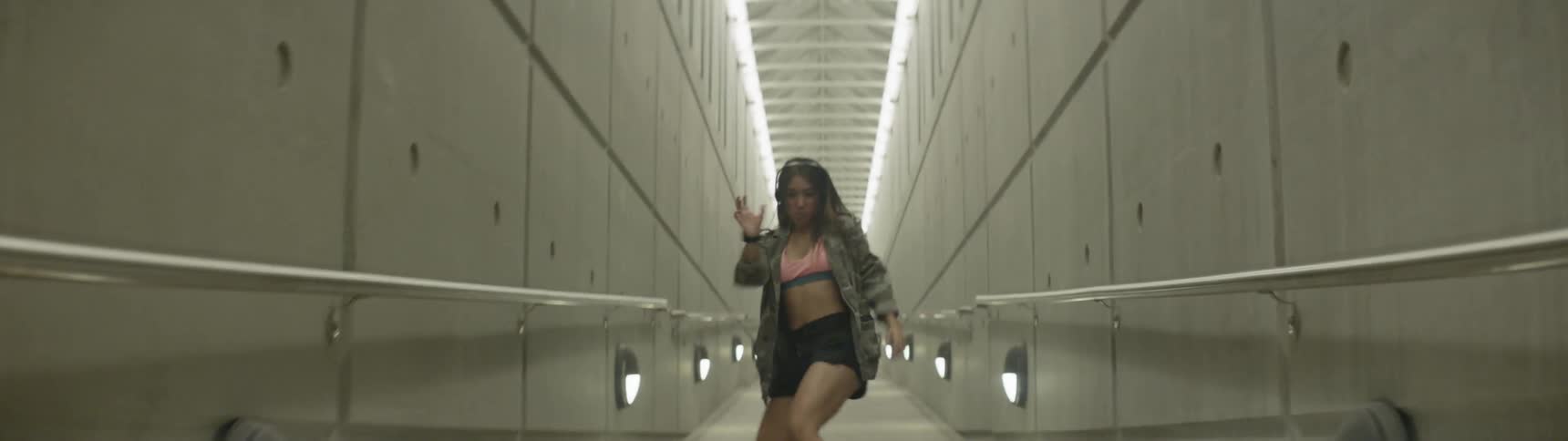 A woman in a narrow hallway dancing while listening to music on headphones