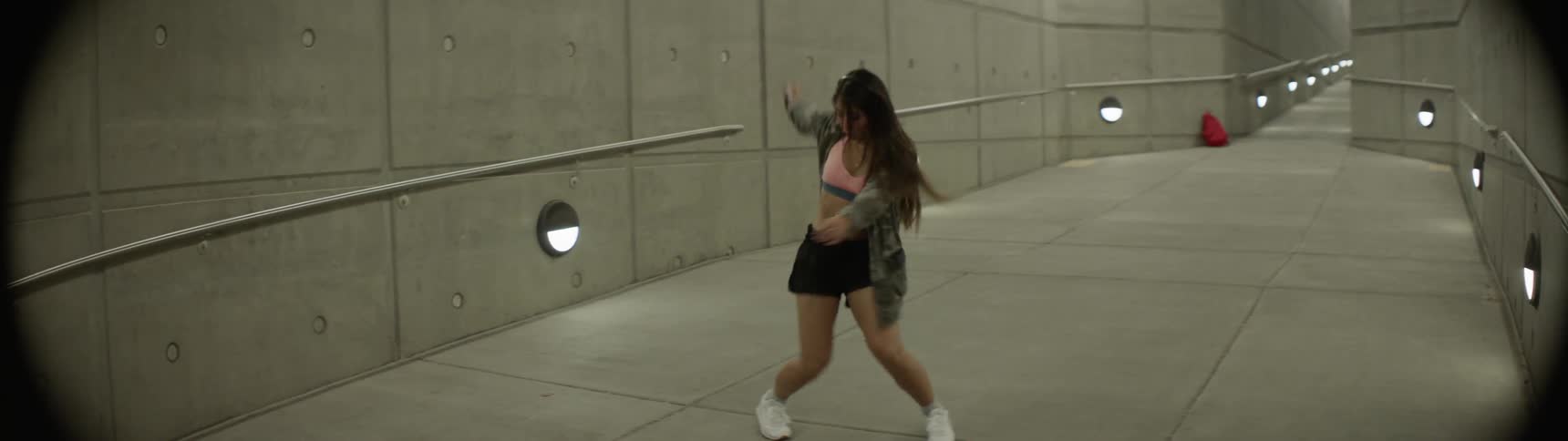 A woman dances in a cement corridor