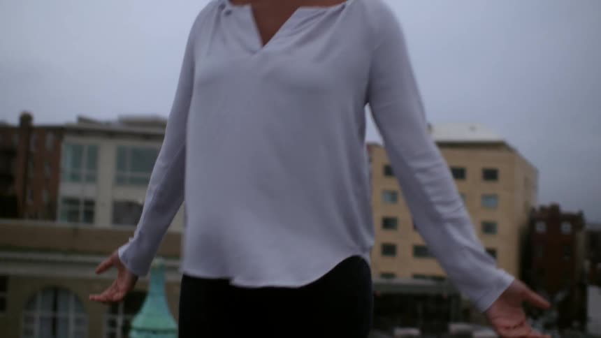 Woman spinning and then stretching towards a cloudy sky in a city