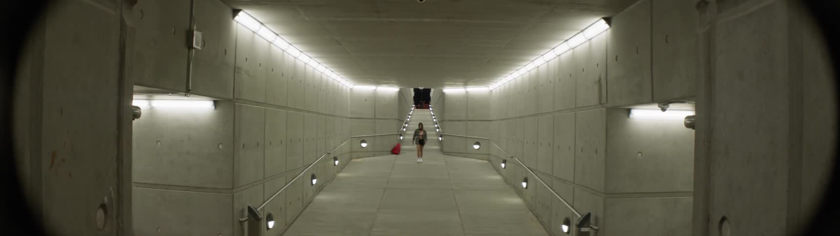 A woman walking down a long well lit concrete tunnel