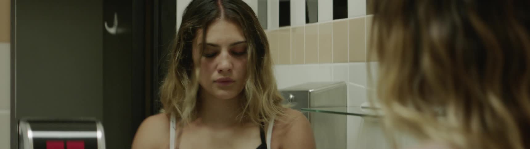 A young girl wipes her eyes in front of a mirror