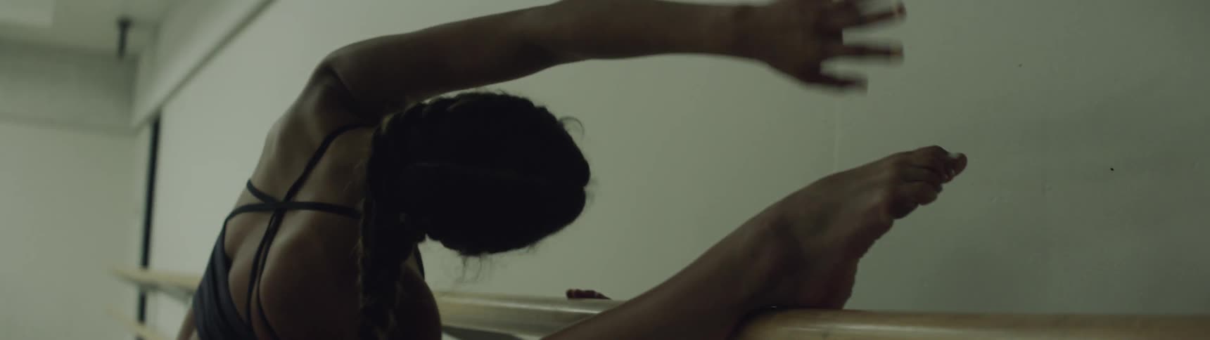 A thin but muscular woman has her leg up on a rail mounted to a wall as she stretches her arm above her head