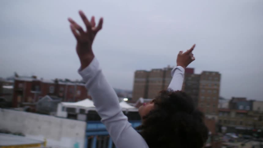 A woman raises her arms in the air on a roof on a cloudy day