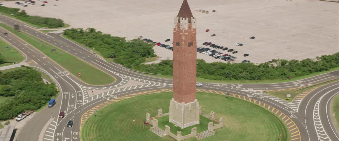 A long road leads directly toward and then curves around a historical monument that is a tall tower