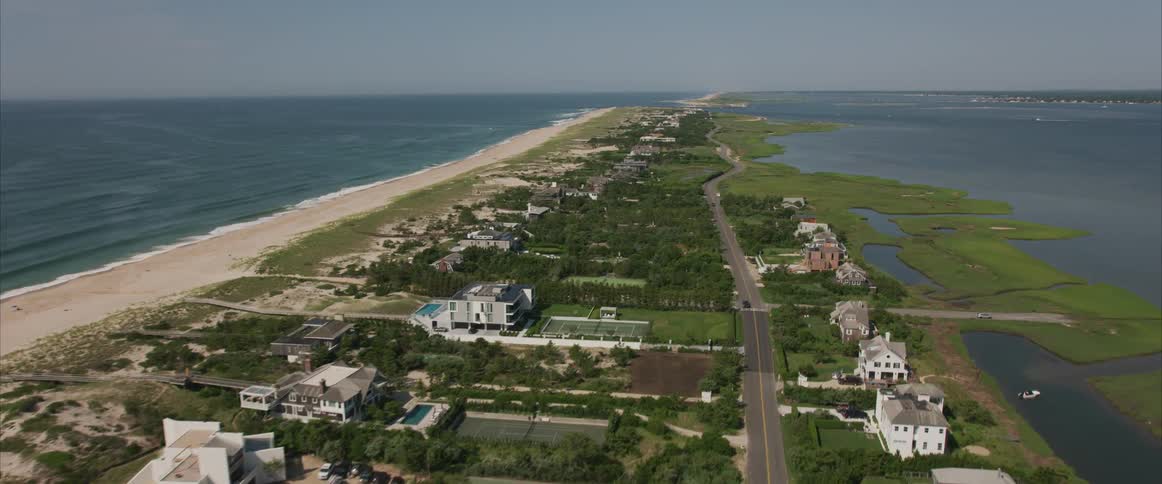 A long narrow peninsula is lined with a very long stretch of sandy beach on one side as well as a chain of large and luxurious residences
