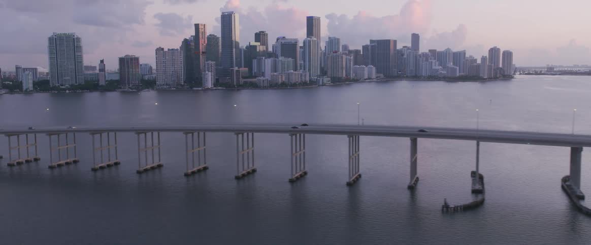 A large metropolitan area with many skyscrapers on the waterfront can been seen across from a long bridge and island