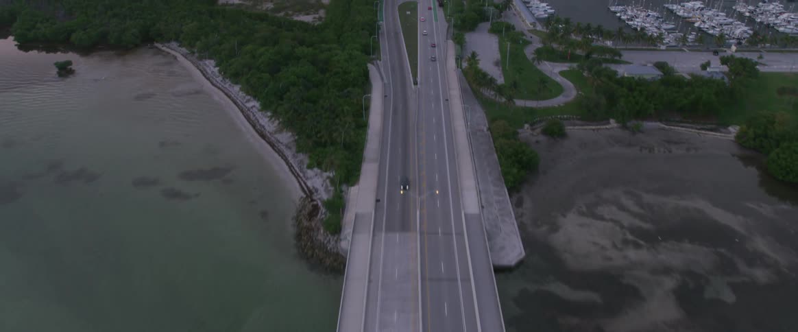 Cars drive along long bridge over ocean