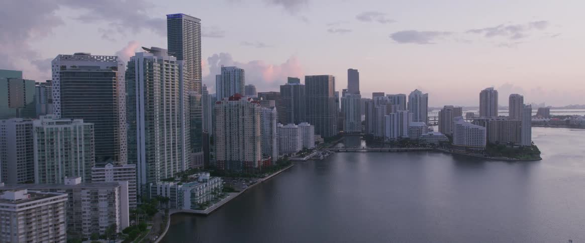 An aerial view of a city skyline next to a large body of water at dawn with pinkish clouds in the distance