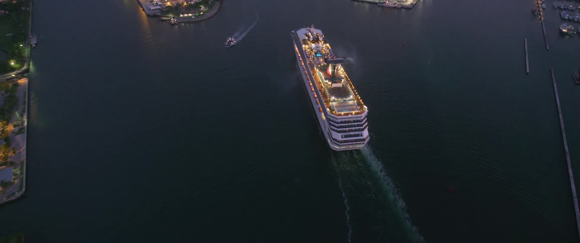 Camera flies over a large cruise ship in a harbor