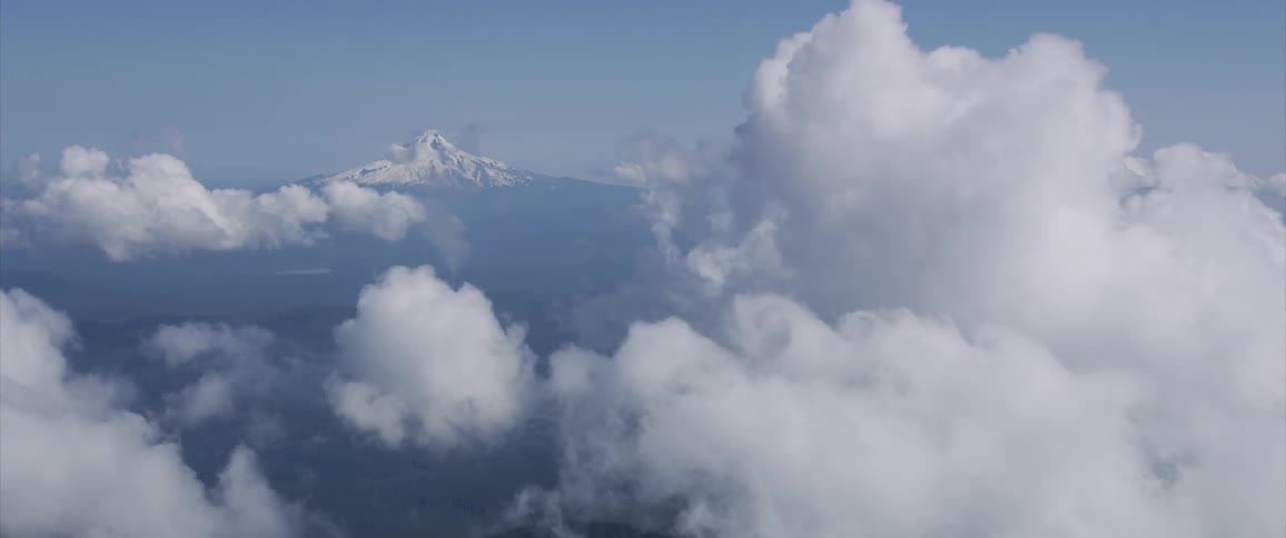 The camera flies near clouds looking towards a mountain