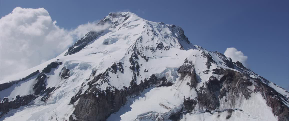 Landscape of snowy mountain surrounded by clouds with blue sky during daylight
