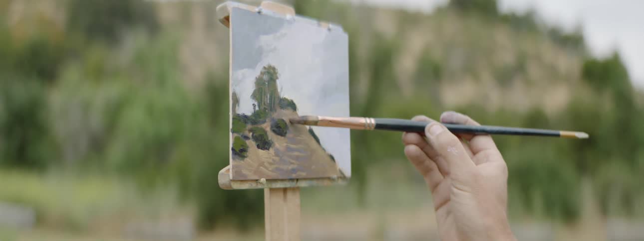 A man making a landscape painting outdoors during the day