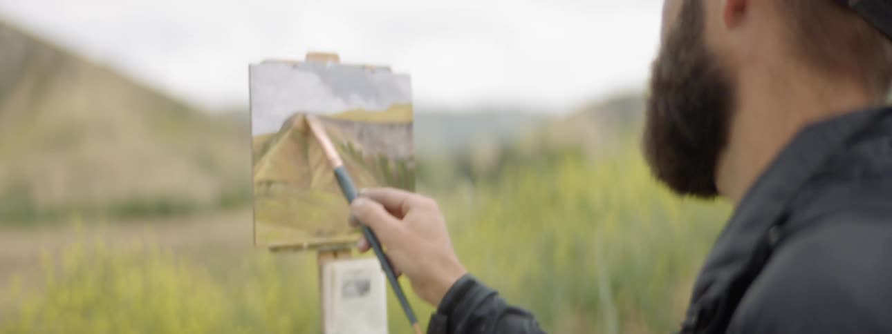 A man outside painting the scenery on a canvas