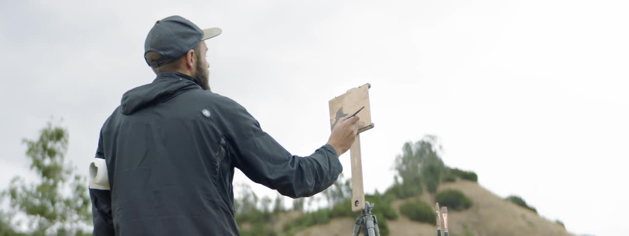 Man painting outdoors on a small canvas