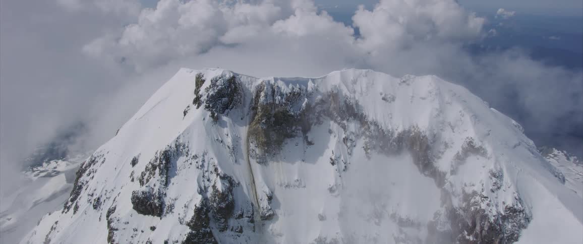 A mountain peak surrounded by clouds and covered in snow
