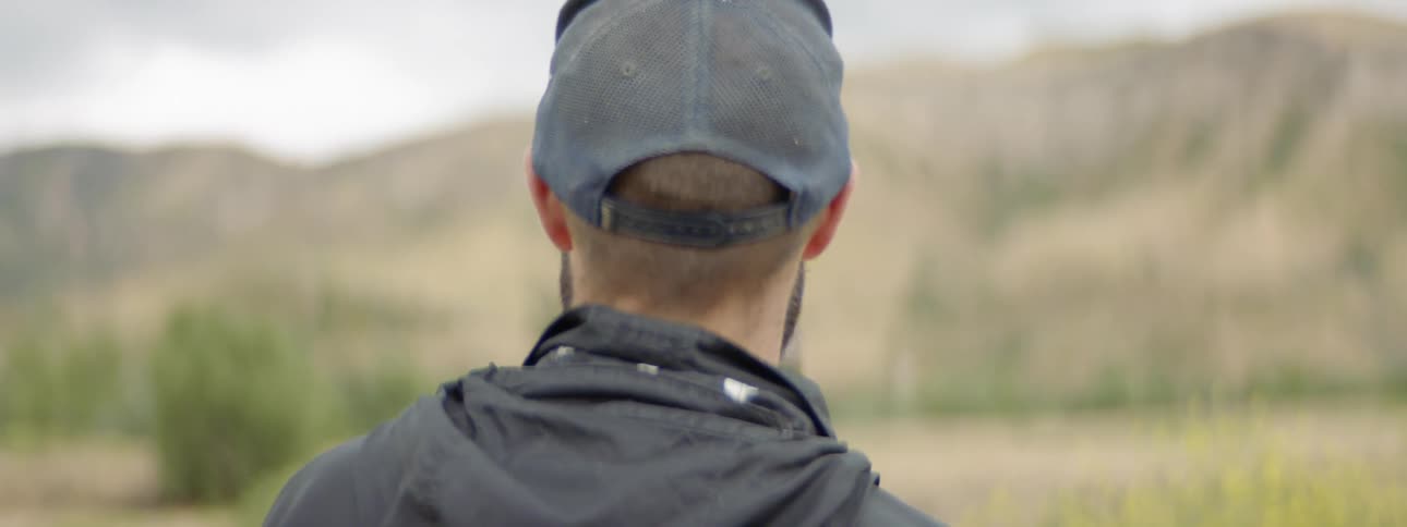 Man wearing cap paints picture of a landscape with mountains during daylight
