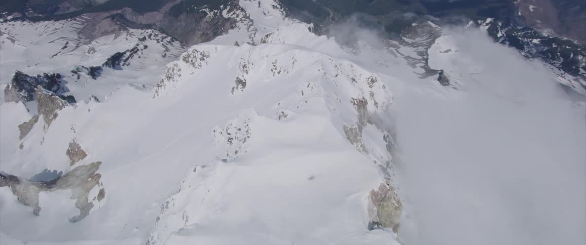 Skyline of the snowy mountain top surrounded by clouds during daylight