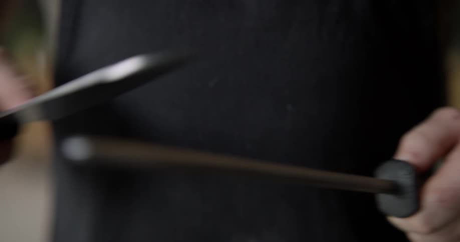 A Caucasian man uses a sharpening stick to sharpen a kitchen knife in a kitchen.