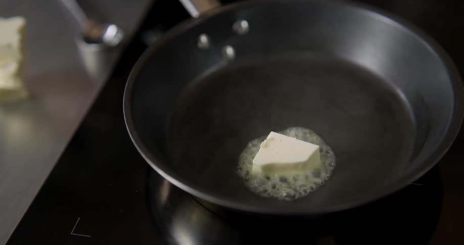 Melting butter sizzles and bubbles in a close-up shot of a skillet.