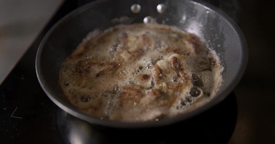 Food cooks in pan with boiling gravy sauce in close-up shaky and slowed down shot.