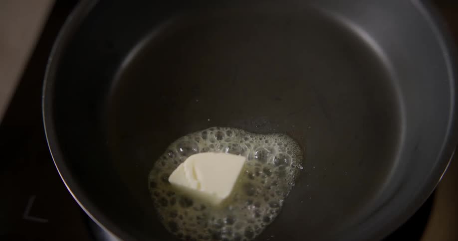 Someone cooks butter in a shaky medium shot in an indoor kitchen during the daytime.