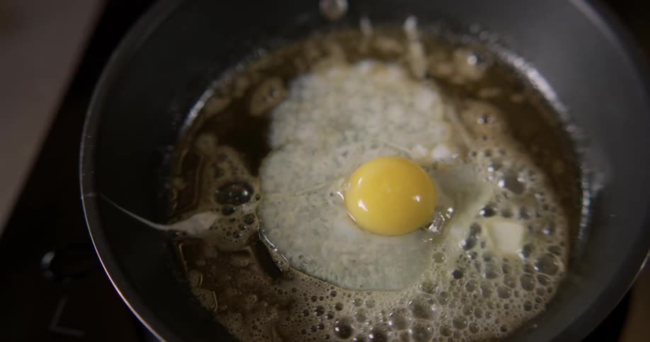 Person frying an egg in a pan with bubbling butter.