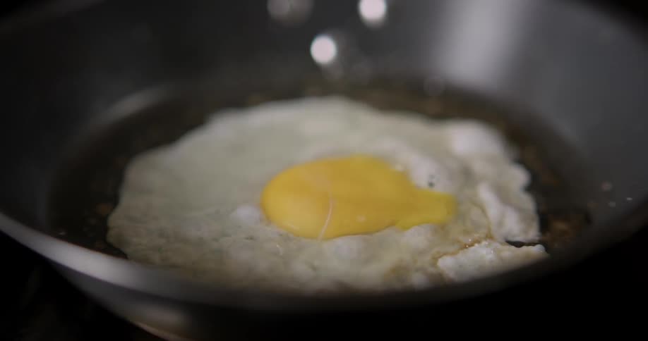 Boiling and sizzling Egg in a tight close-up shot on a frying pan.