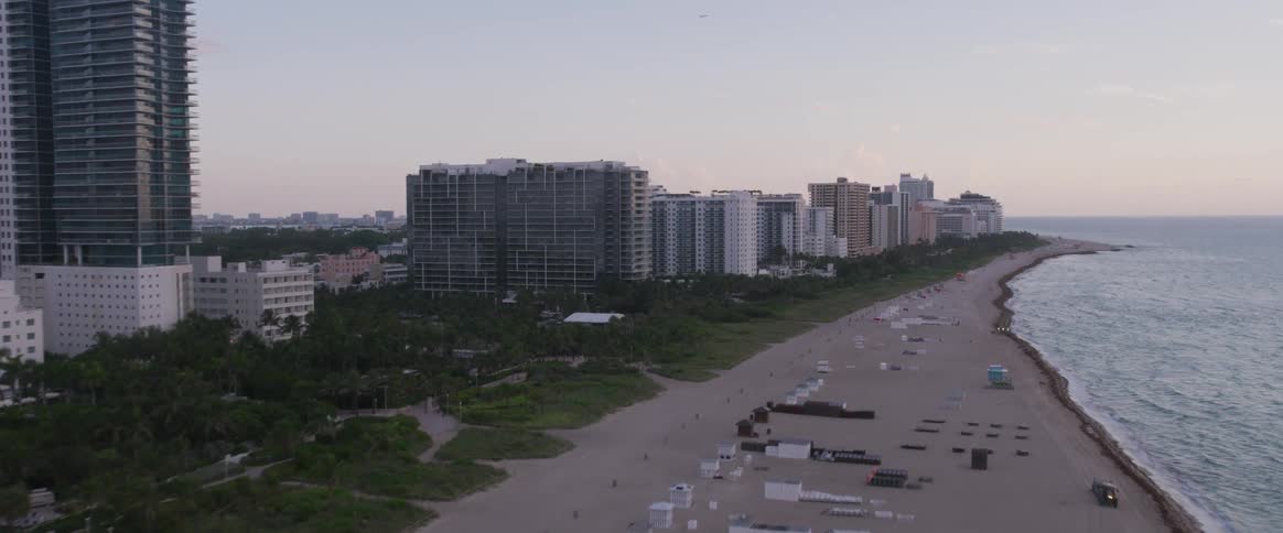 The camera flies over a beach next to a city