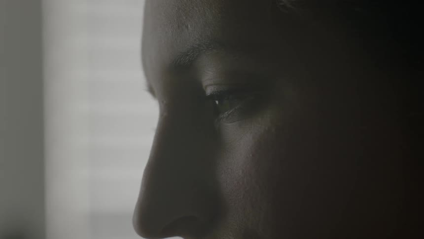 A woman slowly opens her eyes in a dark room