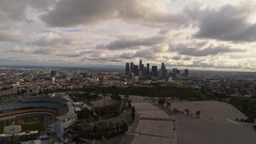 Aerial view of downtown LA with a ball field and parking lot under dramatic storm clouds.