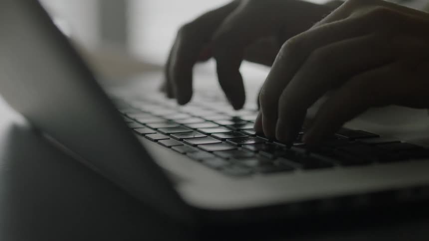 A young woman sits at her desk typing on her laptop
