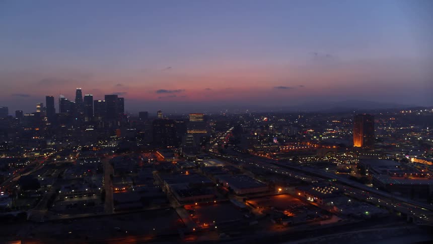 Cars drive on a bridge into and out of a lit up city at sunset