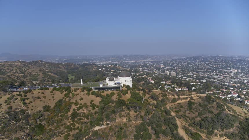A large white building with a unique dome is perched high atop a mountain overlooking an expansive city