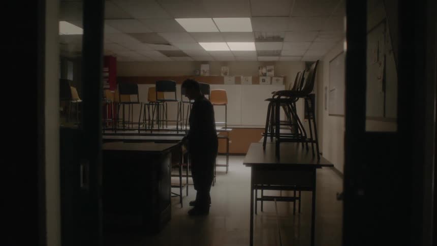 Janitor puts chairs on desks in classroom at closing