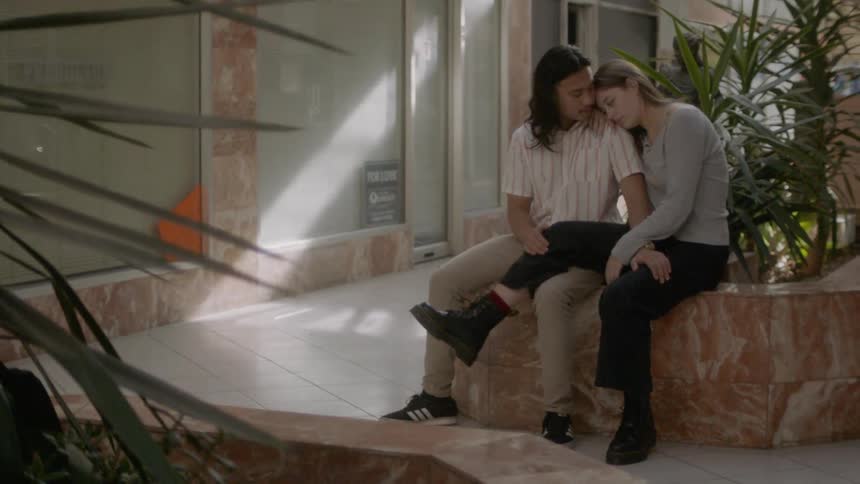 A man and woman cuddling while sitting on a planter in a building