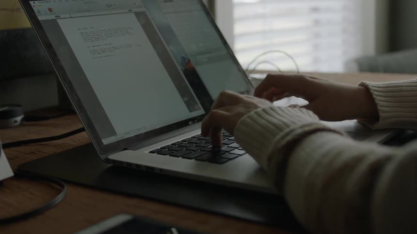 A person is typing at a laptop by the window
