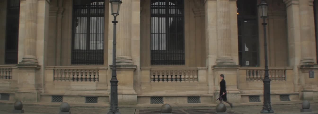 A woman carrying an umbrella walking past a large building