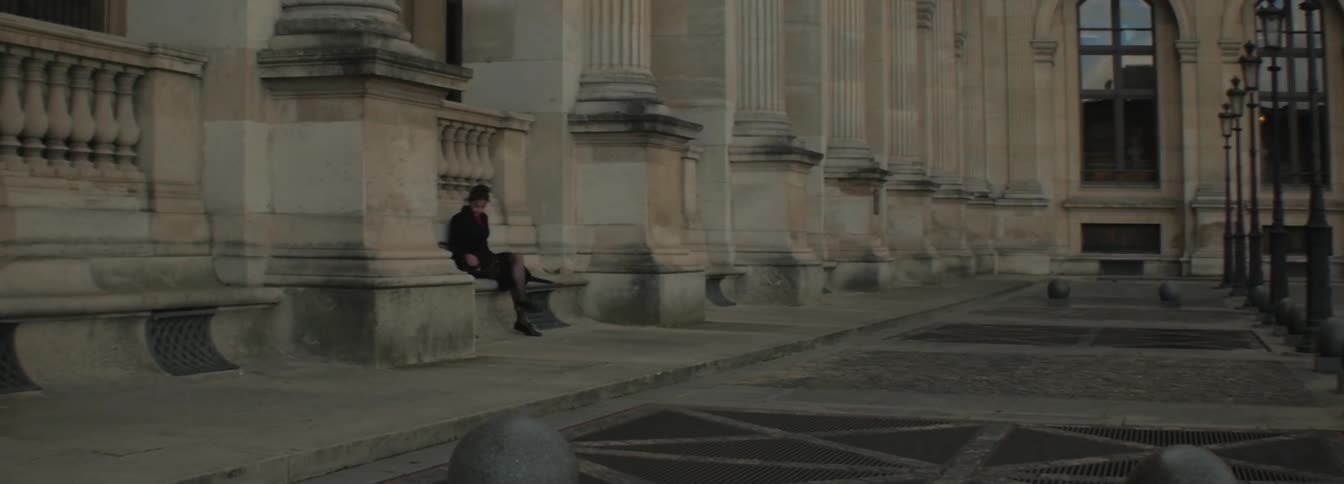 A person sits down on a bench outside a large building